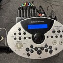 Stříbrný modul elektronických bicích s modrým displejem a značkou Millenium a označením modelu MPS-600. Na horní straně jsou zapojeny početné kabely…