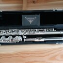 Stříbrná flétna v černém etuiku. Na krabičce uvnitř etuiku je nápis SANKYO FLUTES JAPAN LTD. Nástroj vykazuje mírné známky opotřebení povrchu v podob…