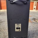 Zadní strana černého reproduktoru s dvěma úchopy a kovovými rohy. Uprostřed je umístěn štítek s nápisy BOSE, TRANSPORT STEER COLUMN a 500 V X RESONAT…