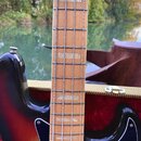 Detailní záběr na hриф a tělo basové kytary s barvou sunburst. Hриф je vyroben ze světlého dřeva s bílými vložkami pražců. Tělo má černý pickguard a…