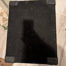 Fotografie zachycuje spodní stranu černého hudebního komba potaženého texturovaným materiálem. V rozích jsou umístěny čtyři černé plastové nožičky s…