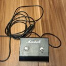 Černý kytarový pedál značky Marshall s dvěma stoupacími spínači. Nad spínači jsou nápisy Channel a Reverb. K pedálu je přiložen černý kabel s konekto…