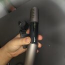 Na fotografii je v ruce držený šedý kovový předmět cylindrického tvaru s rýhovanou horní částí. Střední část je otevřená a odhaluje vnitřní mechanism…