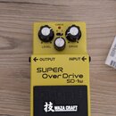 Žlutý kytarový efekt s nápisy SUPER Over Drive SD-1w a logem BOSS. Na horní části jsou tři bílé ovládací knoflíky s popisky LEVEL a DRIVE, přepínač S…