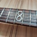 Detail hředu strunového nástroje s tmavým dřevěným hmatníkem a kovovými pražičkami. Na osmém pražci je bílá polohová značka ve tvaru číslice 8. Povrc…