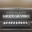 Černý kytarový zesilovač s nápisem MEZZABARBA CUSTOM AMPLIFICATION. Přední panel obsahuje ovládací knoflíky s popisky Input, Brite, Drive, Overdrive,…