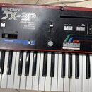 Černý polyfonní syntetizátor s bílými a černými klávesami. Na předním panelu je nápis Roland JX-3P PROGRAMMABLE PRESET POLYPHONIC SYNTHESIZER. Nástro…