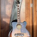 Akustická kytara s vyřezem (cutaway) v provedení sunburst. Na hlavě je nápis Epiphone a na hradle se nachází štítek s textem GUARANTEED Lifetime Warr…
