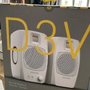 Kartonová krabice s produktem Adam Audio. Na přední straně je žlutý nápis D3V a fotografie dvou bílých studiových monitorů s nápisem ADAM AUDIO. V do…