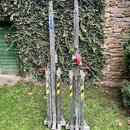 Na fotografii jsou dva kovové zvedací stojany s červenými klikami a horními svěrkami. Na levém stojanu je modrý nápis WORK. Povrch kovu vykazuje znám…