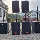 Sada černých reproduktorů značky JBL. V dolní řadě stojí šest subwooferů, dva z nich jsou umístěny na stojanech. Na dvou horních reproduktorech a vše…