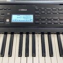 Černý digitální klavír značky YAMAHA s bílými a černými klávesami. V horní části je umístěn modrý LCD displej s textem 001 L!CGrPno a 00180sGtPop. Ko…