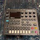 Digitální syntetizátor Elektron Digitone v šedé barvě. Na horní části je nápis Polyphonic Digital Synthesizer a logo Elektron. Zařízení obsahuje disp…