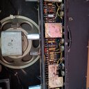 Fotografie zachycuje vnitřek starého elektronického zařízení, pravděpodobně zesilovače s reproduktorem. Jsou vidět vakuové elektrony, kondenzátory a…