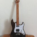 Elektrická kytara s tmavým, pravděpodobně černým lakem s viditelnou strukturou dřeva. Má bílý perleťový pickguard, jeden humbucker u mostu a dva sním…