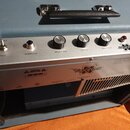 Detail zadní strany kytarového zesilovače v modrém vinylu s kovovým ovládacím panelem. Na panelu jsou nápisy ON, POWER, REVERB, TONE, VOLUME a BRIGHT…