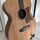Akustická kytara s přímým průřezem v těle, vyrobená z dřeva s viditelnou strukturou zrna. Kytara má tmavý hmatník, tmavý pickguard a černý kobylník s…