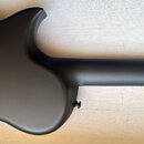 Detail těla a hředu černého hudebního nástroje s matným povrchem. Na fotce nejsou viditelné žádné značky, loga ani nápisy. Povrch je hladký a bez vid…