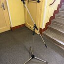 Kovový mikrofonní stojan s triumfovým rozbočovačem a tříramennou základnou. Povrch je stříbrný, s černými plastovými knoflíky a koncovkami nožic. Na…