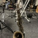 Fotografie zachicuje saxofon v kovovém, stříbrném provedení. Nástroj je umístěn na stojanu v interiéru s kabeláží a dalšími hudebními komponenty v po…