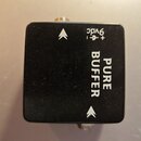 Černý kytarový pedál s hranatým tvarem. Na povrchu je bílý nápis PURE BUFFER a označení napájení + - 9vdc. Vedle textu jsou dvě bílé šipky směřující…