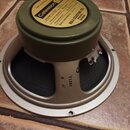 Fotografie zachycuje zadní stranu reproduktoru s olivově zeleným magnetem a béžovým rámem. Na žlutém štítku je uveden nápis Celestion, Model number G…
