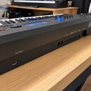 Černý digitální klavír s nápisem MODX8 na pravém boku. Na zadní straně jsou viditelné konektory s popisky USB TO HOST a USB TO DEVICE. Nástroj je umí…