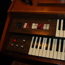 Dřevěný elektronický organ se dvěma klávesnicemi. Na ovládacím panelu je nápis CAROLINE DE LUXE a řada přepínačů s popisky Flute 4, Flute 8, Piccolo…