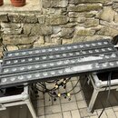 Tři černé lineární LED páse s kulatými světelnými zdroji, umístěné na dvou transportních kufrech. Zařízení jsou propojena černými kabely s žlutými sp…