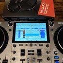 Na fotografii je krabice s černými sluchátky Pioneer DJ HDJ-X5 a stříbrný DJ kontrolér. Na displeji kontroléru je zobrazen software s playlistem skla…