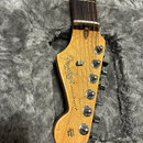 Hlava elektrické kytary z přírodního dřeva s tmavým hmatníkem. Na hlavě je čitelné logo Fender, nápis STRATOCASTER® a text ORIGINAL CALIFORNIA. V dol…