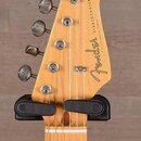 Záběr na hlavu a hриф elektrické kytary z přírodního dřeva. Na zadní straně hlavy je viditelné logo Fender a nápis STRATOCASTER. V horní části hlavy…