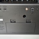 Zadní strana černého elektronického zařízení s několika konektory. Jsou zde nápisy AUX IN, PHONES/REC OUT (pod kterým je text CABINET VOICED) a DC IN…