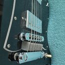 Detail elektrické kytary s tmavě zeleným lakem a černým pickguardem. Je vidět chromovaný hnízdový kobylník, jedna chromovaná humbuckerová snímač a čá…