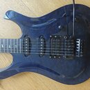 Modrá elektrická kytara s prosvítající strukturou dřeva. Na mostku je nápis Floyd Rose Original. Kytara má dva humbuckery a jeden single-coil snímač,…