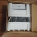 Otevřený hnědý papírový karton s bílým polystyrenovým vložkovým materiálem. Uvnitř je umístěna malá bílá krabička s recyklačním symbolem a nápisem PA…