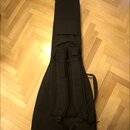 Černý textilní pouzdro na hudební nástroj v tvaru kytary. Na zadní straně jsou dvě nastavitelné ramenní popruhy s polstrováním. Pouzdro je položené n…