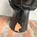 Detail spodní části černého perkusního nástroje s opletením z černých provazů. Povrch je v dolní části výrazně poškozen, kde je vidět rozsáhlý odřesn…