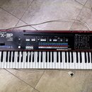 Černý syntetizátor s červeným horním panelem. Na levé straně je bílý nápis Roland a model JX-3P, pod kterým je text PROGRAMMABLE PRESET POLYPHONIC SY…