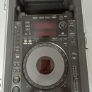 Černý DJ player Pioneer CDJ-900 umístěný v přepravním kufru s pěnovou výplní. Zařízení má velký ovládací jog-wheel, displej a řadu tlačítek s nápisy…