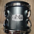 Šedý buben s kovovými obručmi a ladicími šrouby. Na korpusu je nápis Pearl EX EXPORT SERIES DRUMS HEAT COMPRESSION SYSTEM SHELL MADE IN TAIWAN. Povrc…