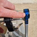 Detailní záběr na modrou kovovou součástku stavu nebo stojanu, kterou ukazuje prst. Na modrém povrchu je viditelný malý odřes nebo stěrka bílé barvy.…