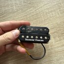 Černý humbucker s kovovými póly. Na spodní části je bílým nápisem značka Seymour Duncan. K snímači vedou černé vodiče, jeden z nich je zakončen žlutý…