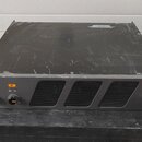 Černý rackový přístroj s kovovým šasi. Na předním panelu jsou dva otočné ovladače pod čísly 1 a 2, tři ventilační mřížky a vypínač s nápisem POWER. V…