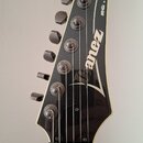 Černá hlava elektrické kytary s bílým lemováním. Na povrchu je bílé logo Ibanez a nápis RG SERIES. Jsou vidět ladicí kolíky a matice strun u můstku,…