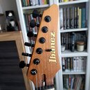 Fotografie zachycuje hlavu elektrické kytary z přírodního dřeva s nápisem Ibanez. Na hlavě jsou umístěny šest ladících kolbíčků černé barvy. Povrch d…