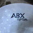 Detailní záběr na povrch kovového činely s koncentrickým žilováním. Uprostřed je černý nápis ABX cymbals. Povrch vykazuje drobné nečistoty a stopy po…