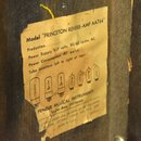 Detail žluté papírové nálepky s technickými specifikacemi, která je nalepená na dřevěný povrch. Na nálepce je text: Model "PRINCETON REVERB-AMP AA764…