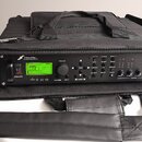 Černý rackový procesor v černé přepravní tašce s popruhem. Na předním panelu je zelený LCD displej a nápisy FRACTAL AUDIO SYSTEMS oraz Axe-Fx ULTRA.…