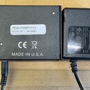 Černý napájecí adaptér a černá kovová krabička s nápisem PEDAL POWER X4 EU a SERIAL No.: 16-30252. Na spodní části krabičky je nápis MADE IN U.S.A. a…